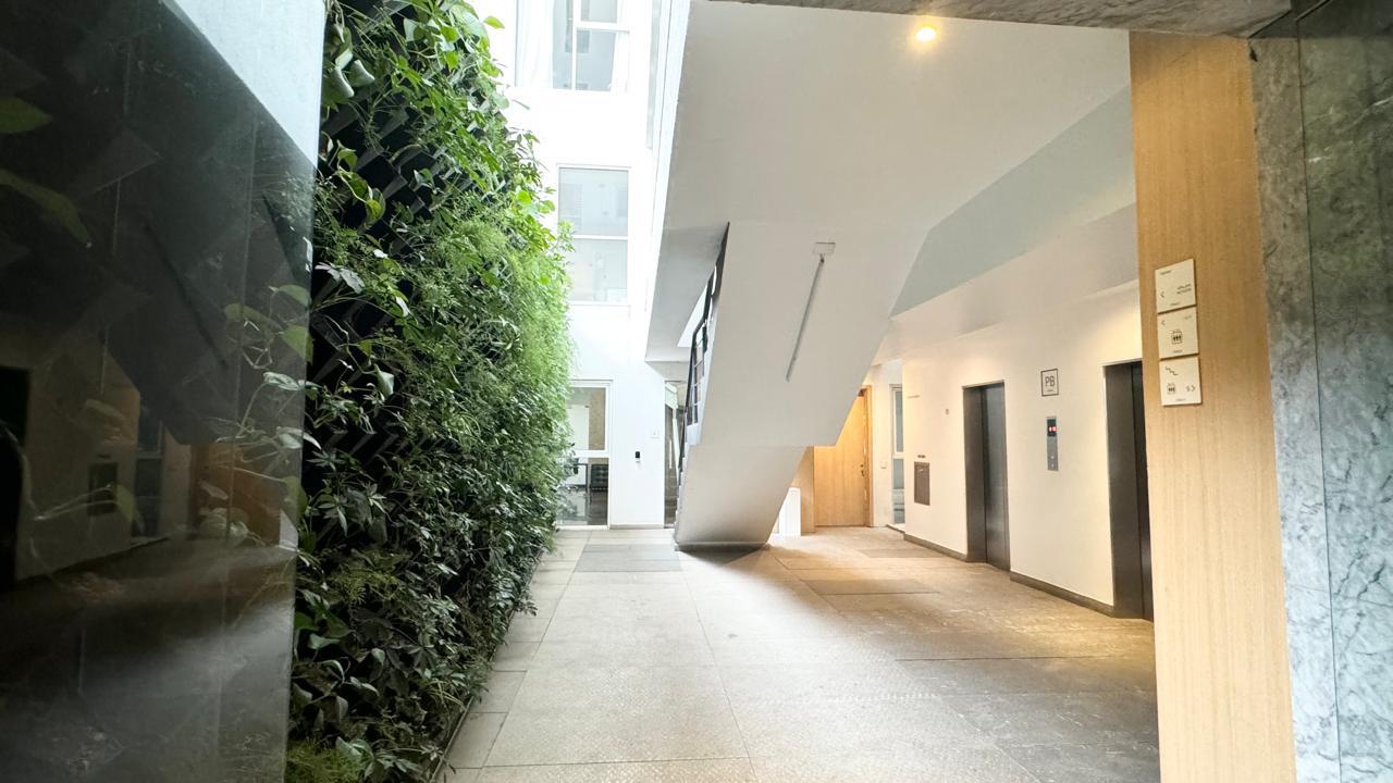 Lobby del edificio con muro verde natural y acceso a elevadores