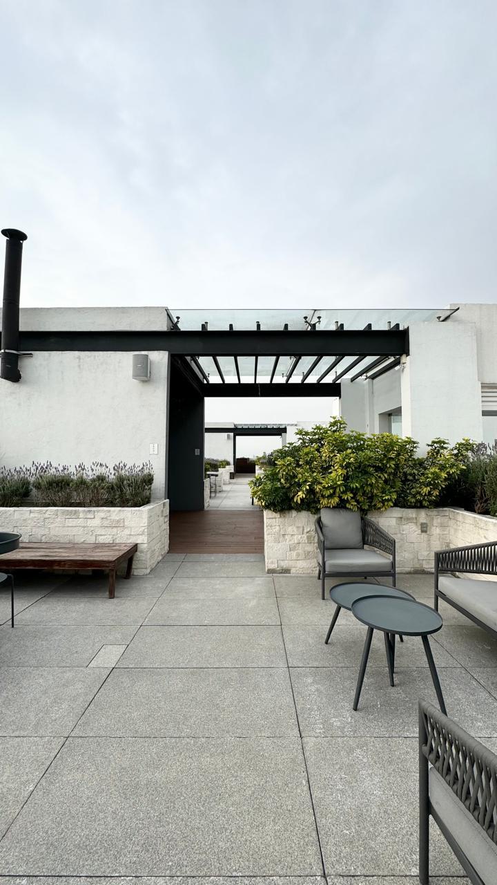 Área común en azotea con pérgola de cristal y mobiliario exterior